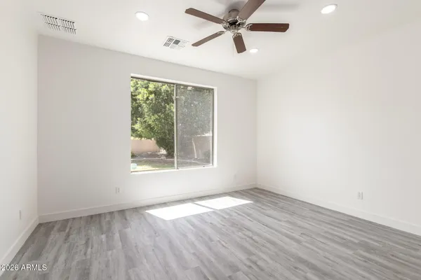 an empty room with wooden floor fan and windows