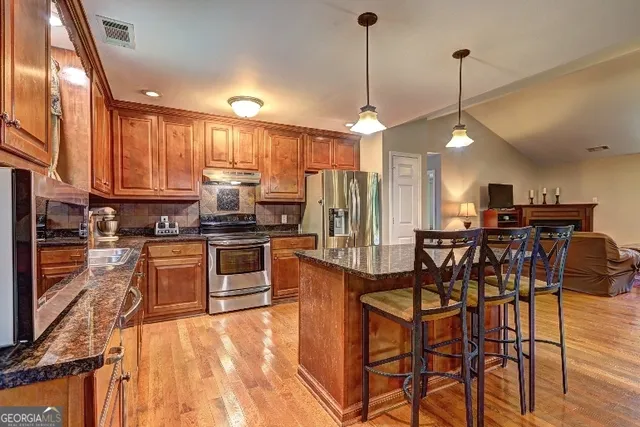 a kitchen with stainless steel appliances kitchen island granite countertop a table chairs and a refrigerator
