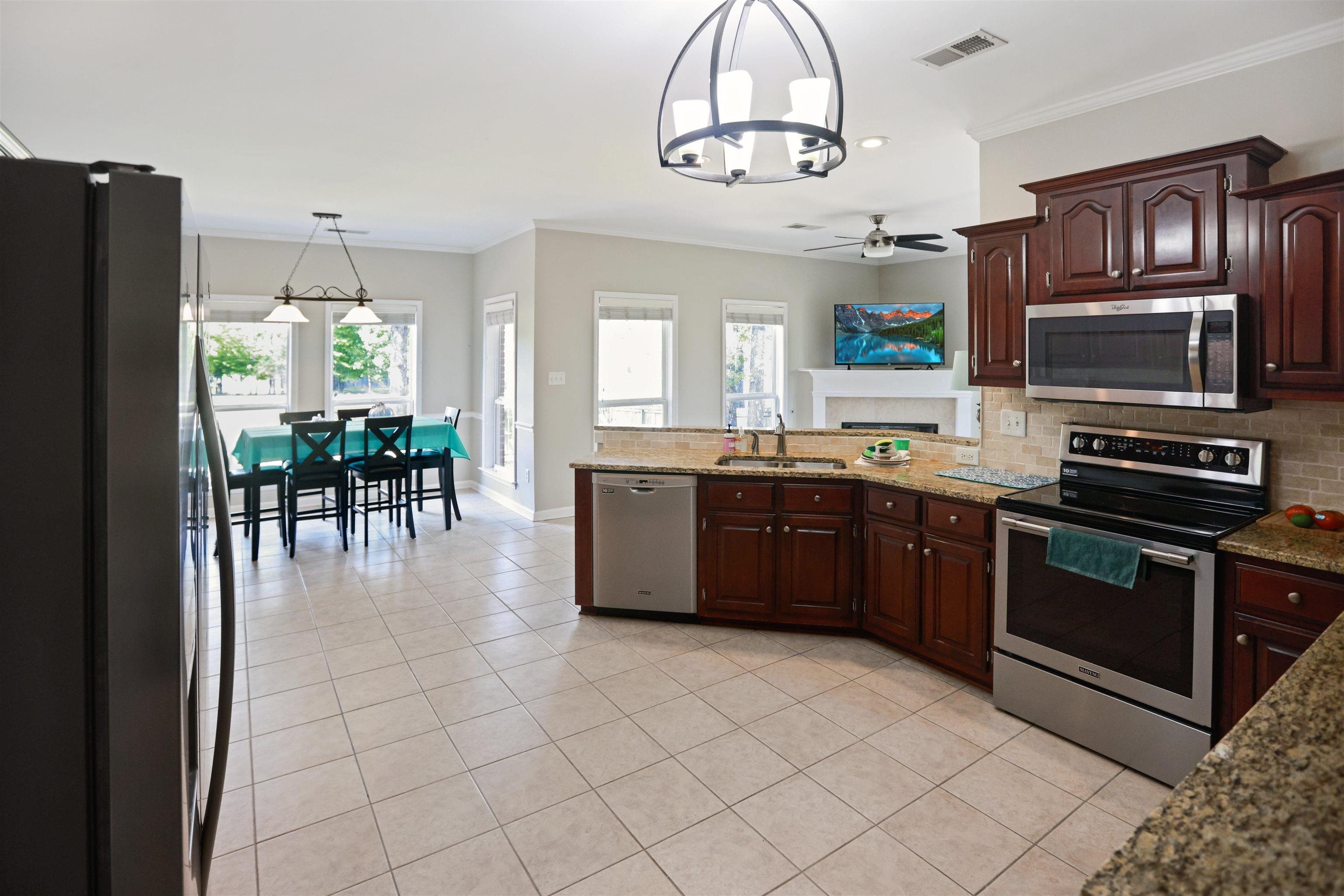 Kitchen featuring appliances with stainless steel finishes, a ceiling fan, decorative backsplash, a peninsula, and light tile patterned flooring