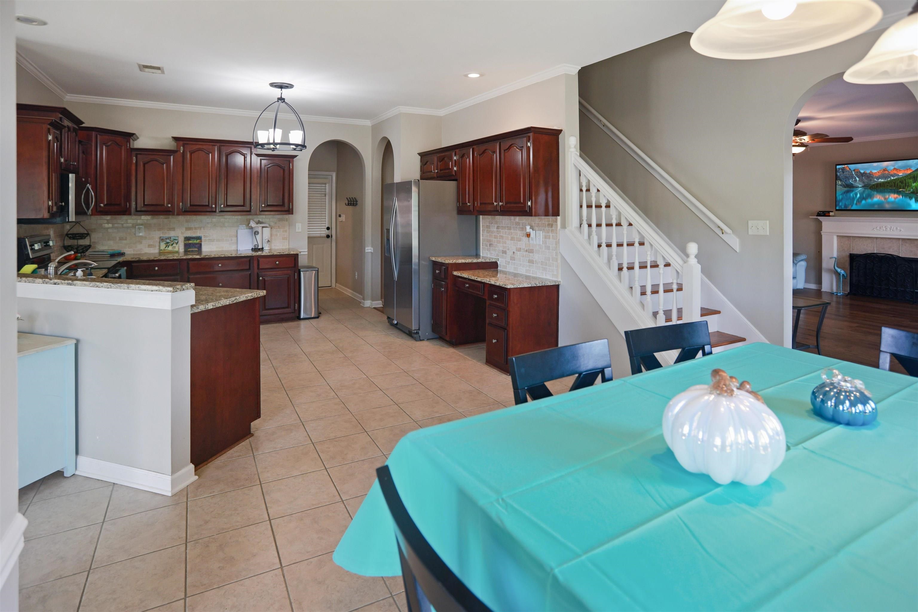 Dining room with arched walkways, ceiling fan, light tile patterned floors, a fireplace, and stairs