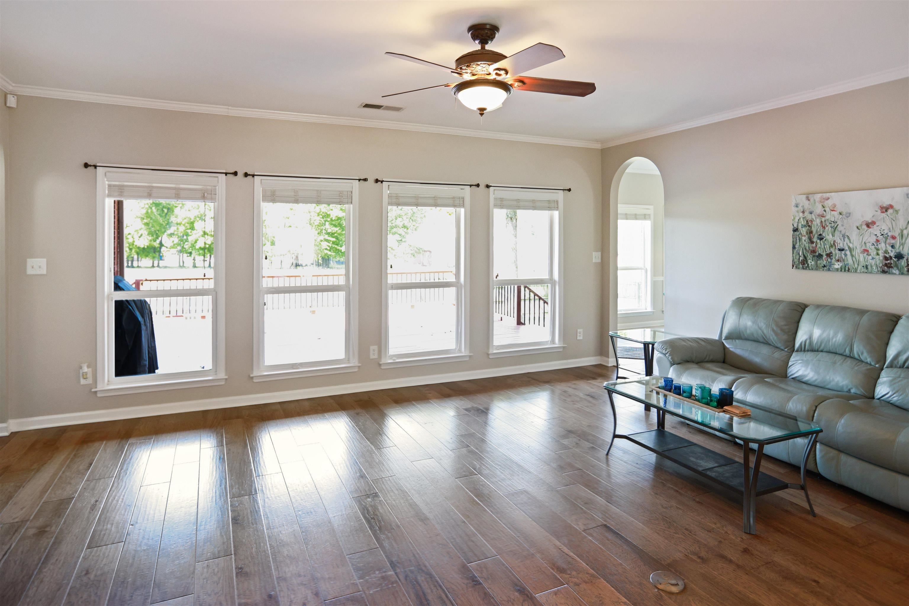 Living room with plenty of natural light, arched walkways, dark wood-style floors, and crown molding