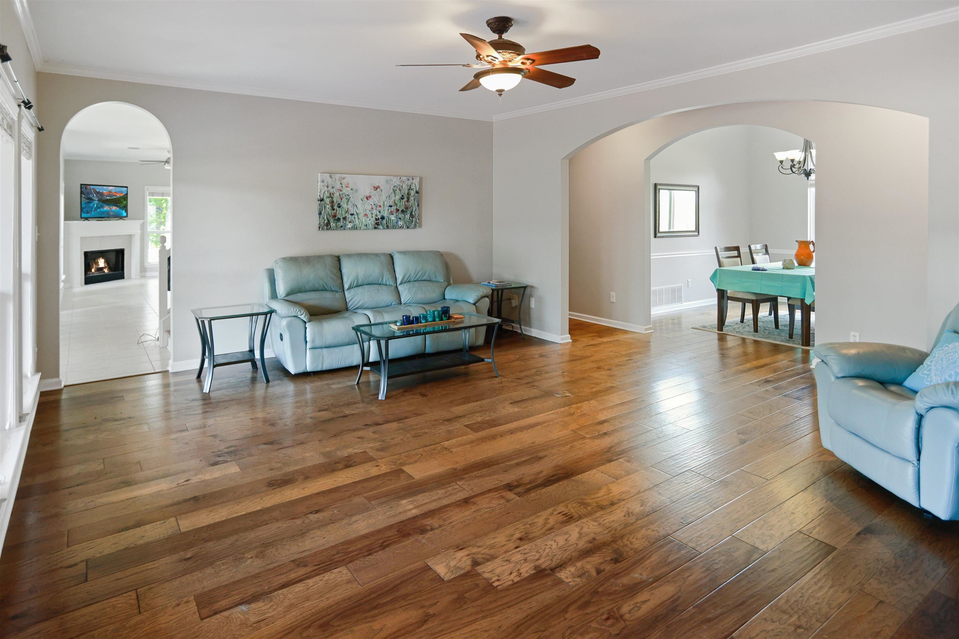 Living area featuring arched walkways, ceiling fan, crown molding, and wood-type flooring