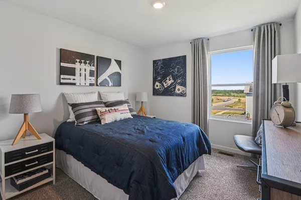 a bedroom with a bed and a lamp on dresser with wooden floor