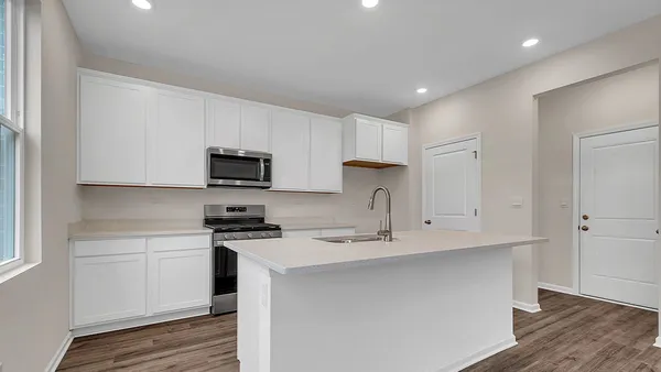 a kitchen with stainless steel appliances a sink a stove a microwave a refrigerator a white cabinets and wooden floor