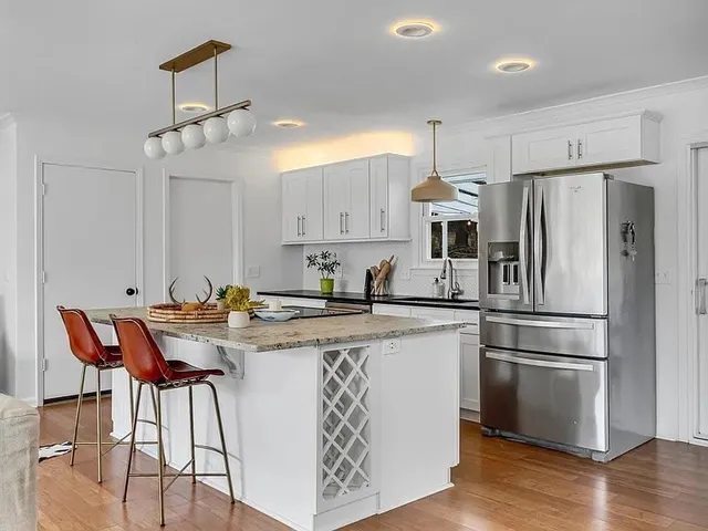 a kitchen with stainless steel appliances granite countertop a refrigerator a sink dishwasher a stove and white cabinets with wooden floor