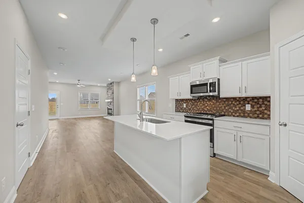 a large white kitchen with a refrigerator a stove top oven a sink dishwasher and white cabinets with wooden floor