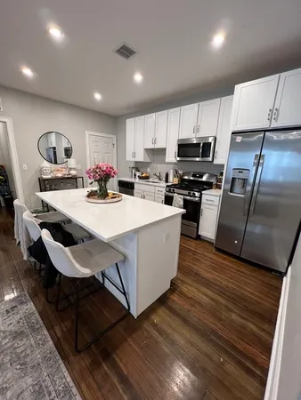 a kitchen with kitchen island a stove a sink a refrigerator wooden floor cabinets and a dining table