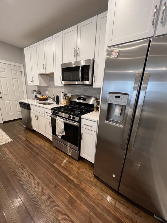 209 East Cottage Street, Unit 1 Boston, MA 02125 - Photo 3 of 10 a kitchen with granite countertop a refrigerator a sink a stove and white cabinets