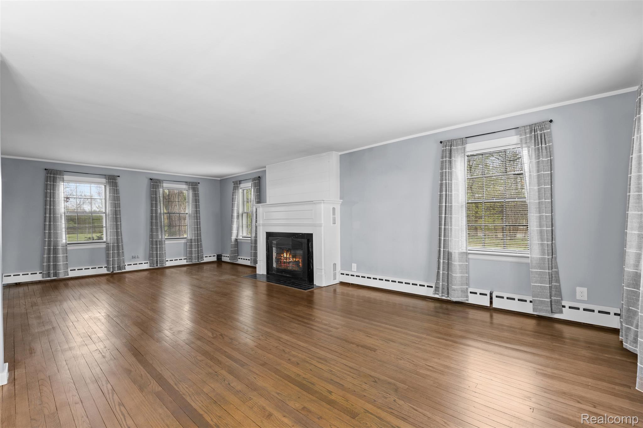 1775 Imlay City Road Lapeer, MI 48446 - Photo 11 of 60 Unfurnished living room with ornamental molding, dark wood-type flooring, a baseboard heating unit, and a fireplace with flush hearth