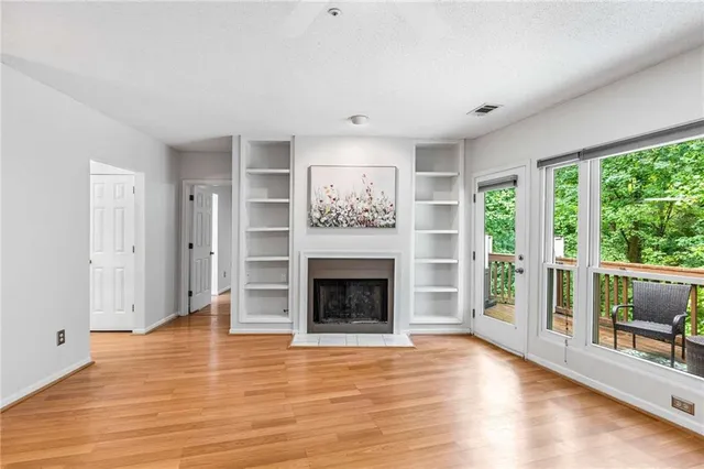 an empty room with wooden floor fireplace cabinet and windows