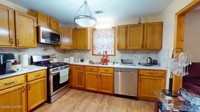 a kitchen with stainless steel appliances granite countertop wooden cabinets a sink a stove a dining table and chairs with wooden floor