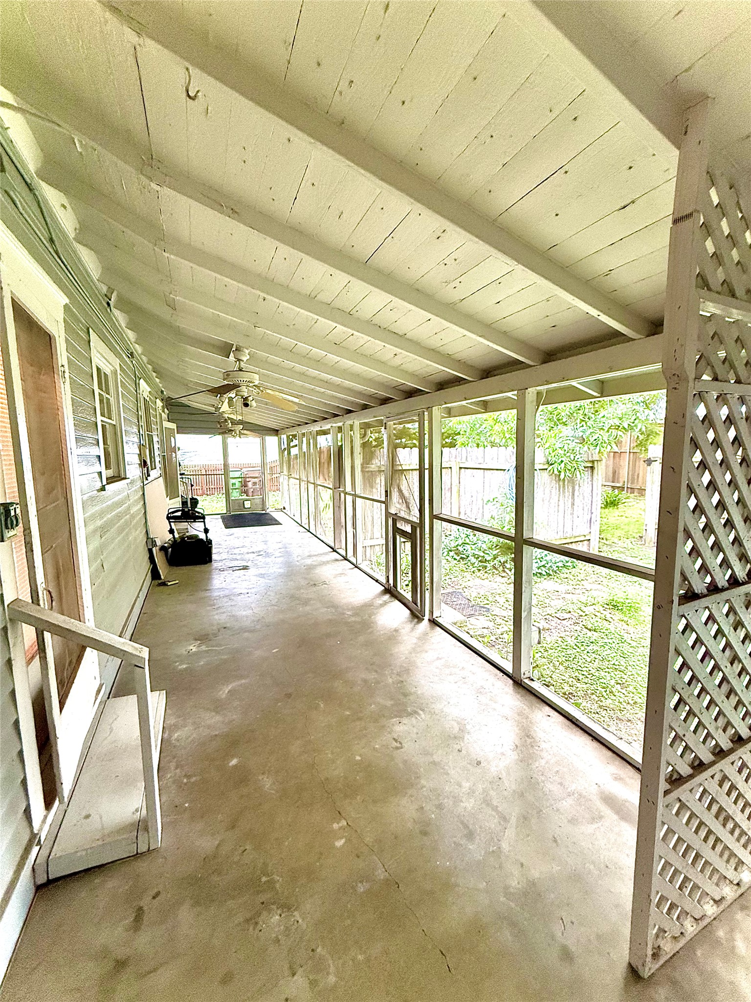 423 South Main Street Lockhart, TX 78644 - Photo 23 of 26 Expansive screened porch featuring a concrete slab, exposed wood beam ceiling, multiple ceiling fans, and wood lattice accents