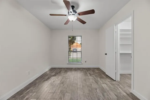 an empty room with wooden floor chandelier fan and windows