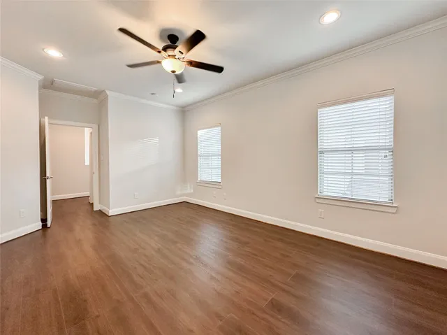 a view of an empty room with wooden floor and a ceiling fan