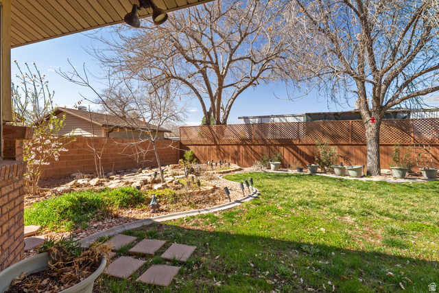 892 Cambridge Drive St. George, UT 84770 - Photo 58 of 65 Expansive backyard featuring a manicured lawn, established trees, a lattice-top privacy fence, a brick retaining wall, and a curved landscape bed