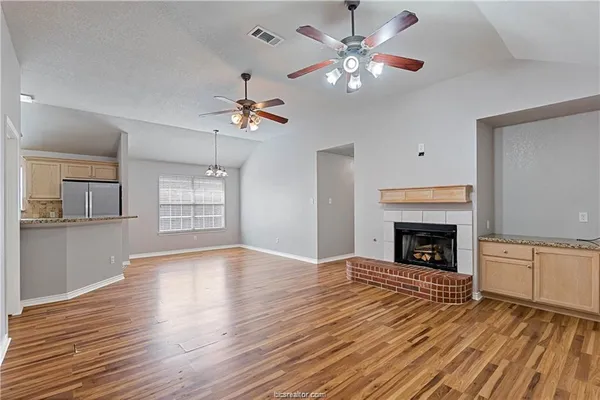 a view of an empty room with a fireplace a ceiling fan and wooden floor