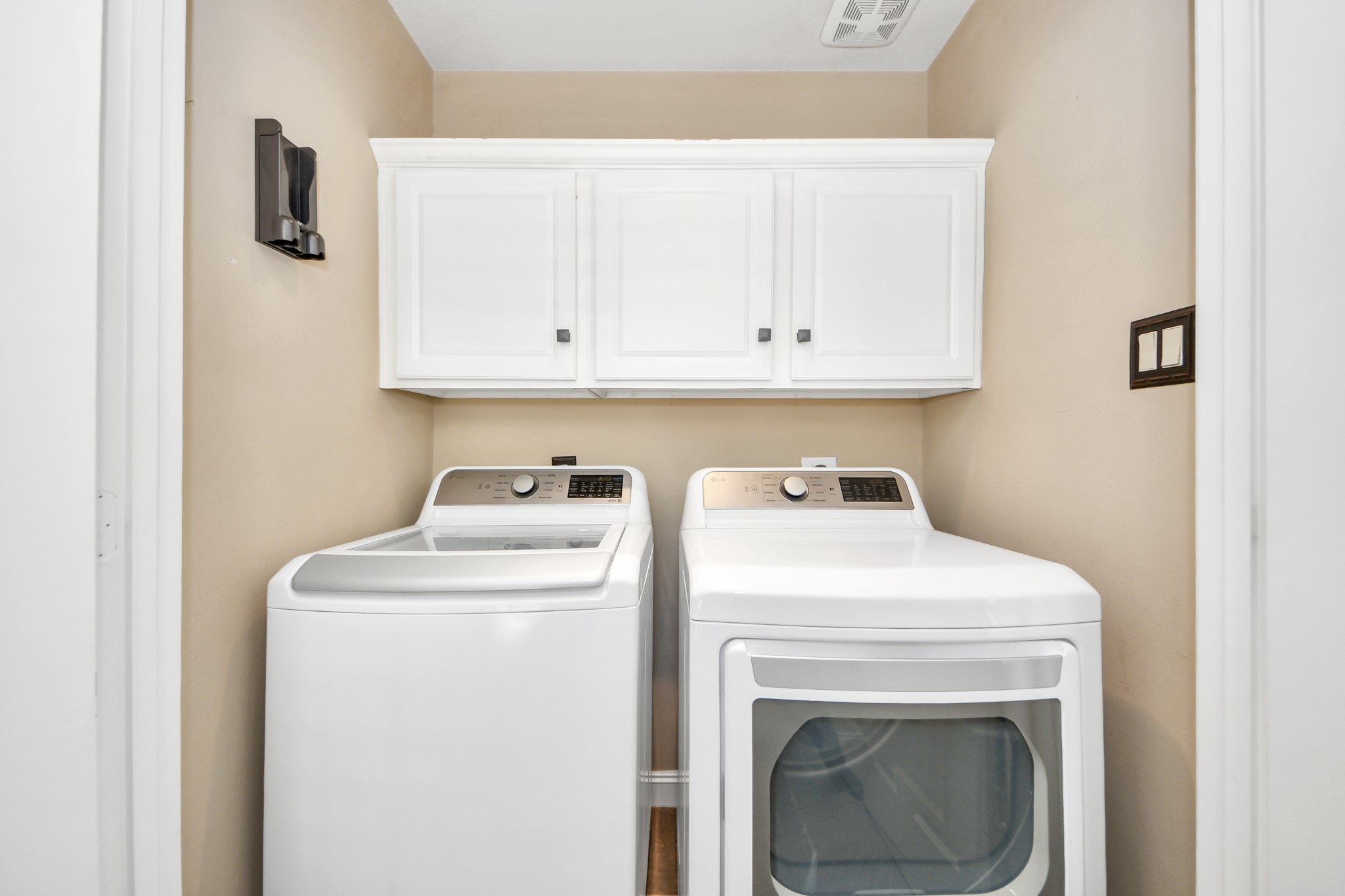 710 Jackson Hill Street Houston, TX 77007 - Photo 21 of 31 Washer and dryer set, topped by white cabinets for storage. The walls are painted in a neutral tone, offering a clean and functional space.