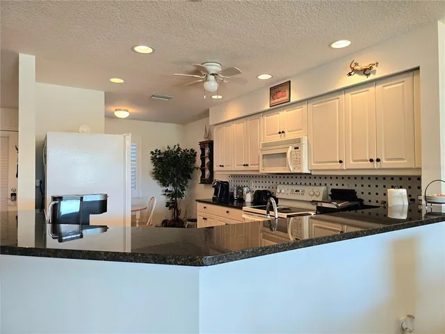 a kitchen with stainless steel appliances granite countertop a sink dishwasher a refrigerator and white cabinets with wooden floor