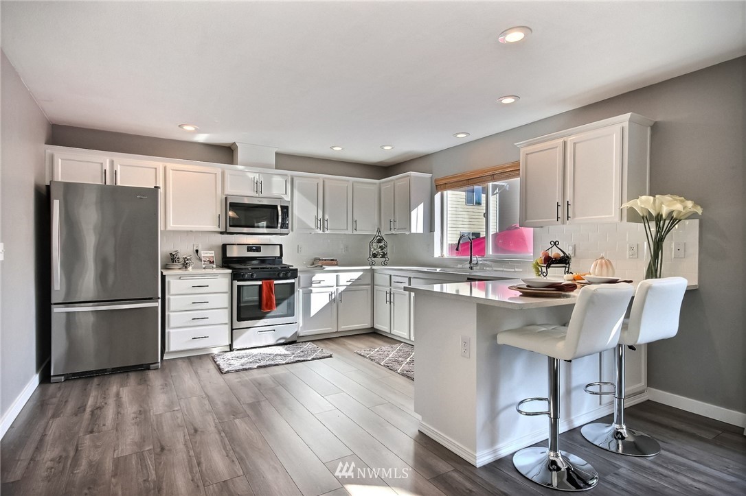 5217 Northeast 11th Street Renton, WA 98059 - Photo 3 of 25 a kitchen with stainless steel appliances a microwave a stove a sink dishwasher a refrigerator and cabinets with wooden floor