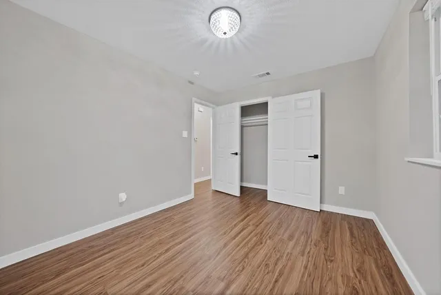 a view of an empty room with wooden floor and a window