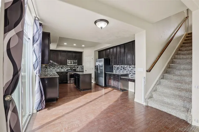 a kitchen with stainless steel appliances kitchen island granite countertop a refrigerator a stove and a sink with wooden floor