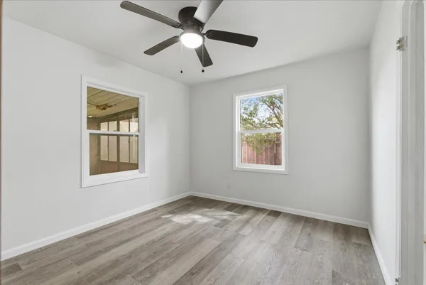 an empty room with wooden floor ceiling fan and windows