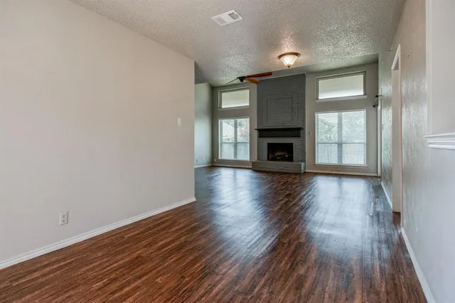 an empty room with wooden floor fireplace and windows