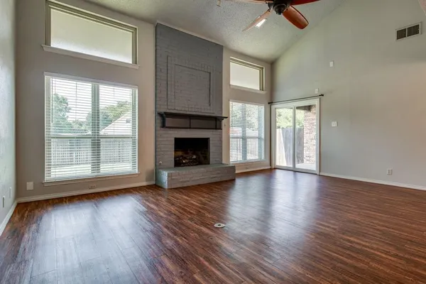 an empty room with wooden floor fireplace and windows