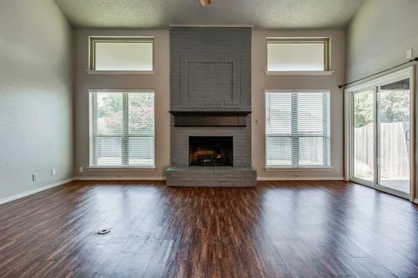 an empty room with wooden floor fireplace and windows