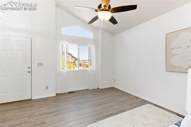 an empty room with wooden floor ceiling fan and windows