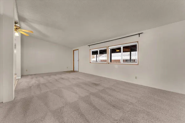 a view of an empty room with window and chandelier fan