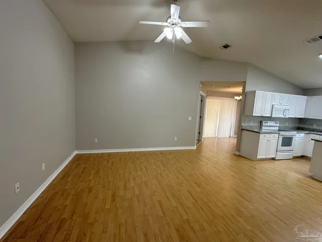 a view of empty room with wooden floor and kitchen view