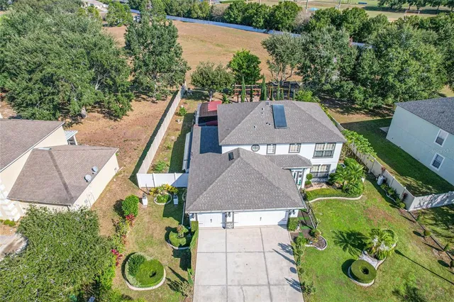 an aerial view of a house with yard and trees in the background