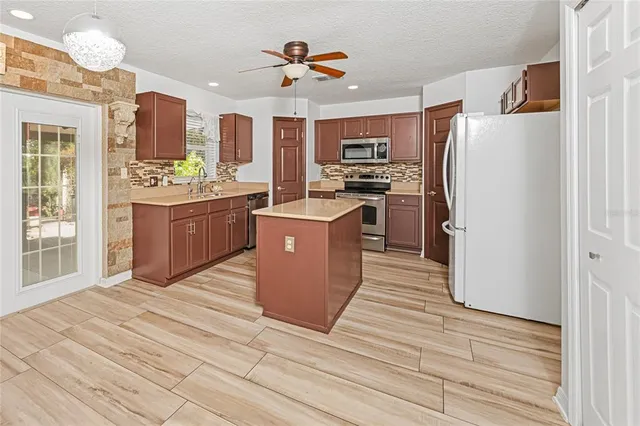 a kitchen with stainless steel appliances kitchen island granite countertop a refrigerator a stove oven a sink dishwasher and white cabinets with wooden floor