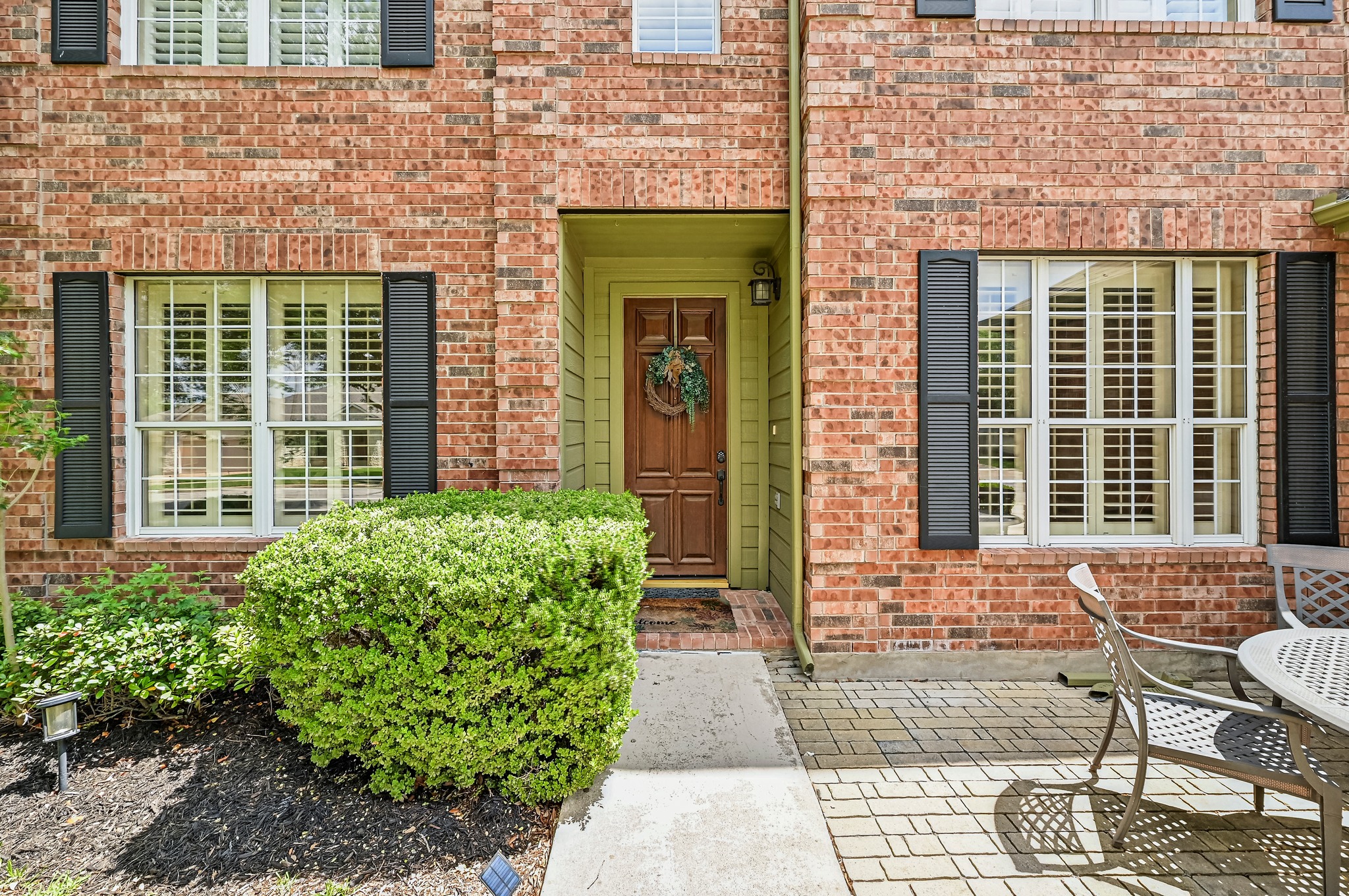2408 Amen Corner Road Pflugerville, TX 78660 - Photo 4 of 40 Brick facade with a warm wood entry door, featuring white window frames with plantation shutters, black louvered shutters, and a paver patio