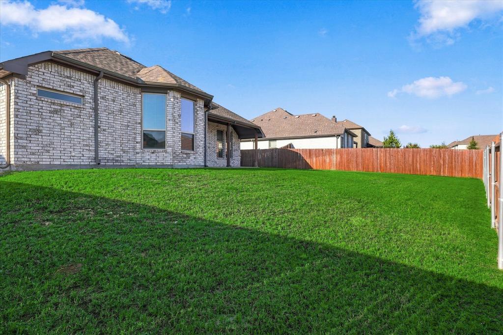 915 Timber Ridge Drive Justin, TX 76247 - Photo 33 of 34 Expansive green lawn with a wood fence, brick exterior, multiple windows, and a shingle roof