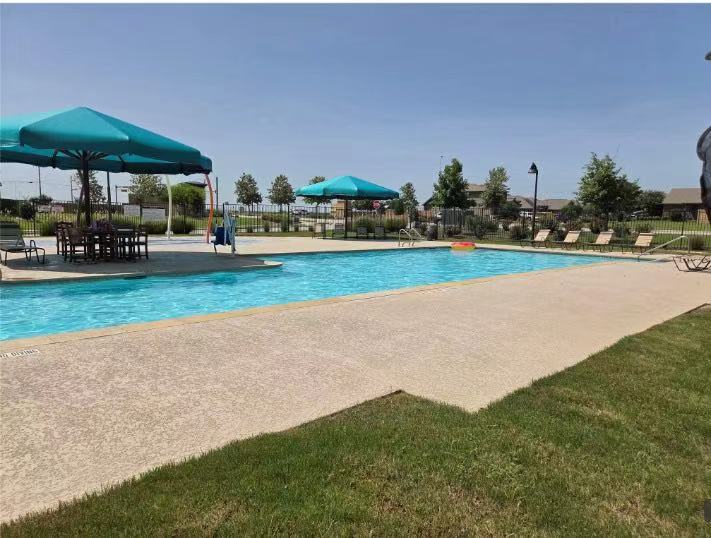 14917 Bajada Rd Manor Manor, TX 78653 - Photo 29 of 31 Expansive community pool area featuring a large swimming pool, surrounding concrete decking, and an adjacent shaded seating area with a table and chairs