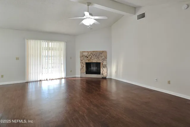 an empty room with wooden floor chandelier fan and windows
