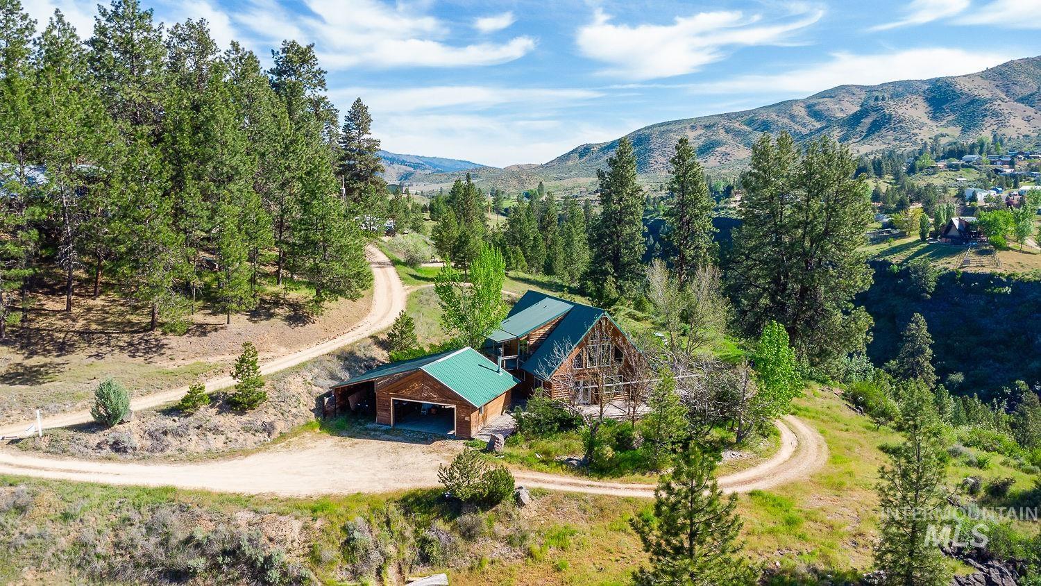42 Hummingbird Haven Road Boise, ID 83716 - Photo 1 of 1 Mountainous terrain with a property featuring a multi-level main residence, a detached garage, and a winding dirt road