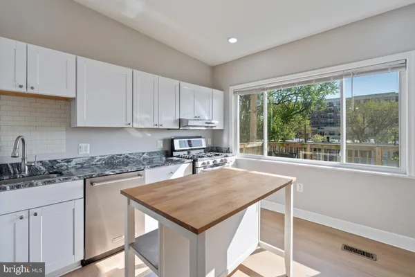 a kitchen with stainless steel appliances granite countertop a stove a sink a refrigerator and white cabinets with wooden floor