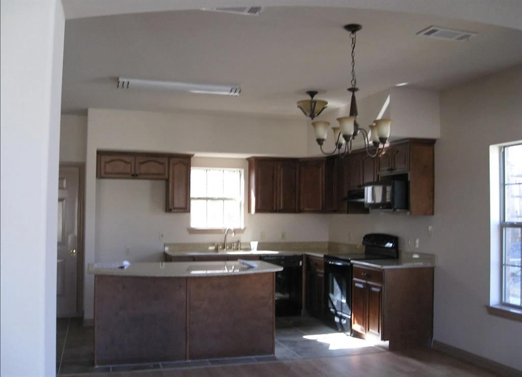 Kitchen featuring dark wood-finish cabinetry, light-toned countertops, a multi-light chandelier, and integrated appliances