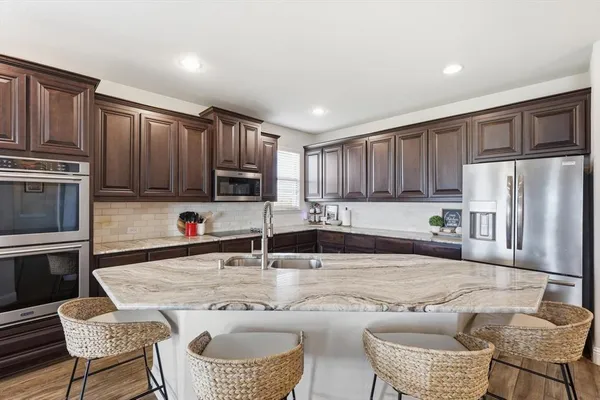 a kitchen with granite countertop a refrigerator oven a sink a stove a dining table and chairs with wooden floor