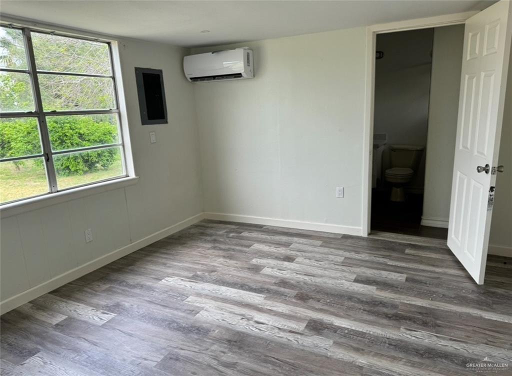 8515 Las Comadres Street Mission, TX 78574 - Photo 6 of 6 Unfurnished bedroom with wood finished floors, a wall mounted air conditioner, electric panel, and ensuite bath