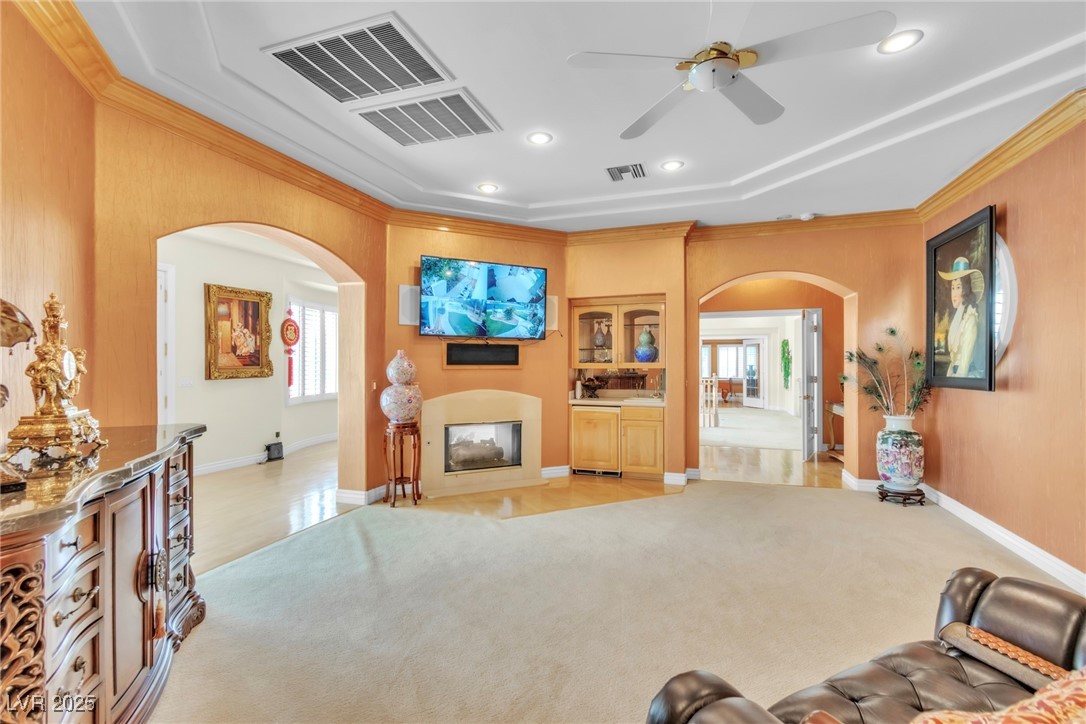 23 Cascade Creek Lane Las Vegas, NV 89113 - Photo 73 of 89 Living area featuring arched walkways, ornamental molding, recessed lighting, light colored carpet, and a glass covered fireplace