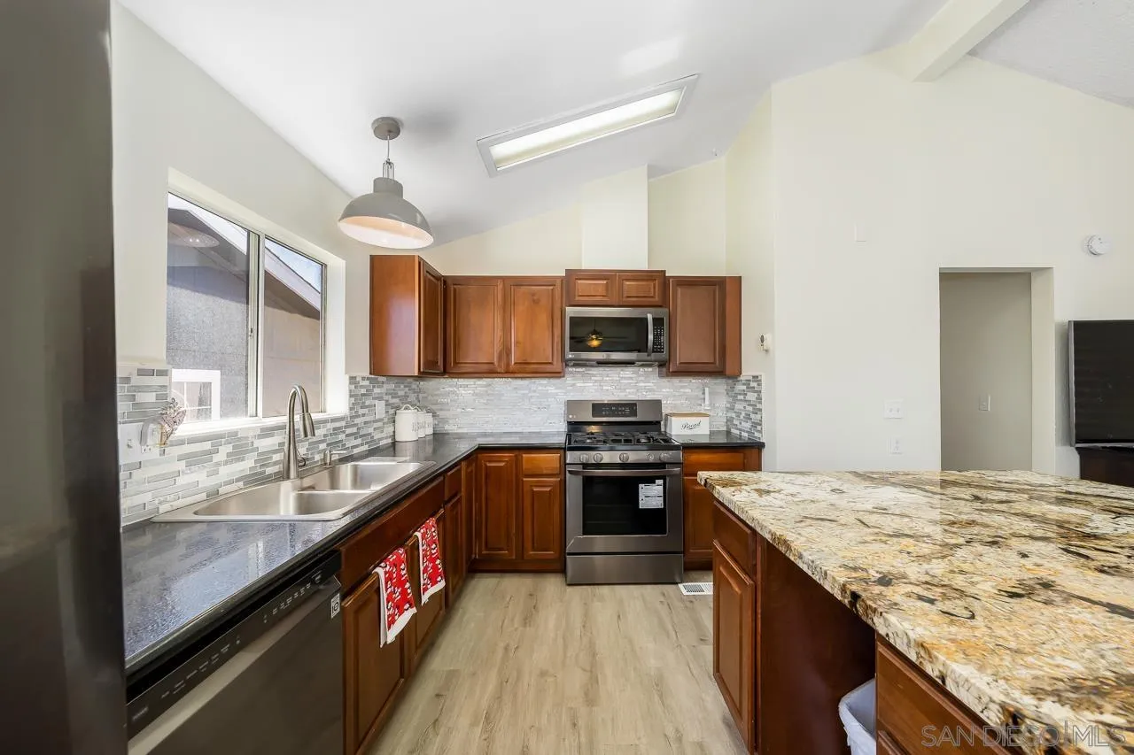 15935 Spring Oaks Road, Unit 201 El Cajon, CA 92021 - Photo 15 of 32 a kitchen with stainless steel appliances granite countertop stove top oven a sink dishwasher a dining table and chairs with wooden floor