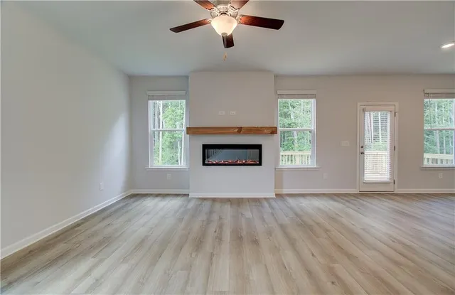an empty room with windows a fireplace a ceiling fan and wooden floor