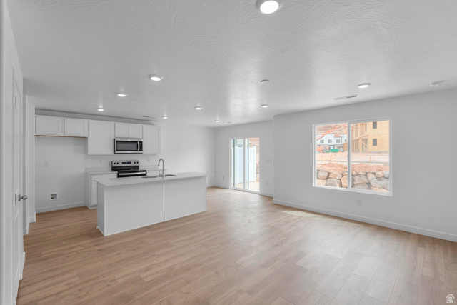 2133 Wolverine Way, Unit 2440 Washington, UT 84780 - Photo 4 of 39 Open-concept living space with light wood-finish flooring, recessed ceiling lighting, and a kitchen featuring white cabinetry and stainless steel appliances