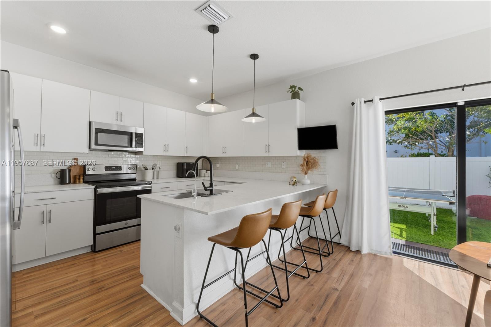 11456 West 33rd Way Hialeah, FL 33018 - Photo 8 of 49 a kitchen with stainless steel appliances a stove a sink a microwave a refrigerator and white cabinets with wooden floor