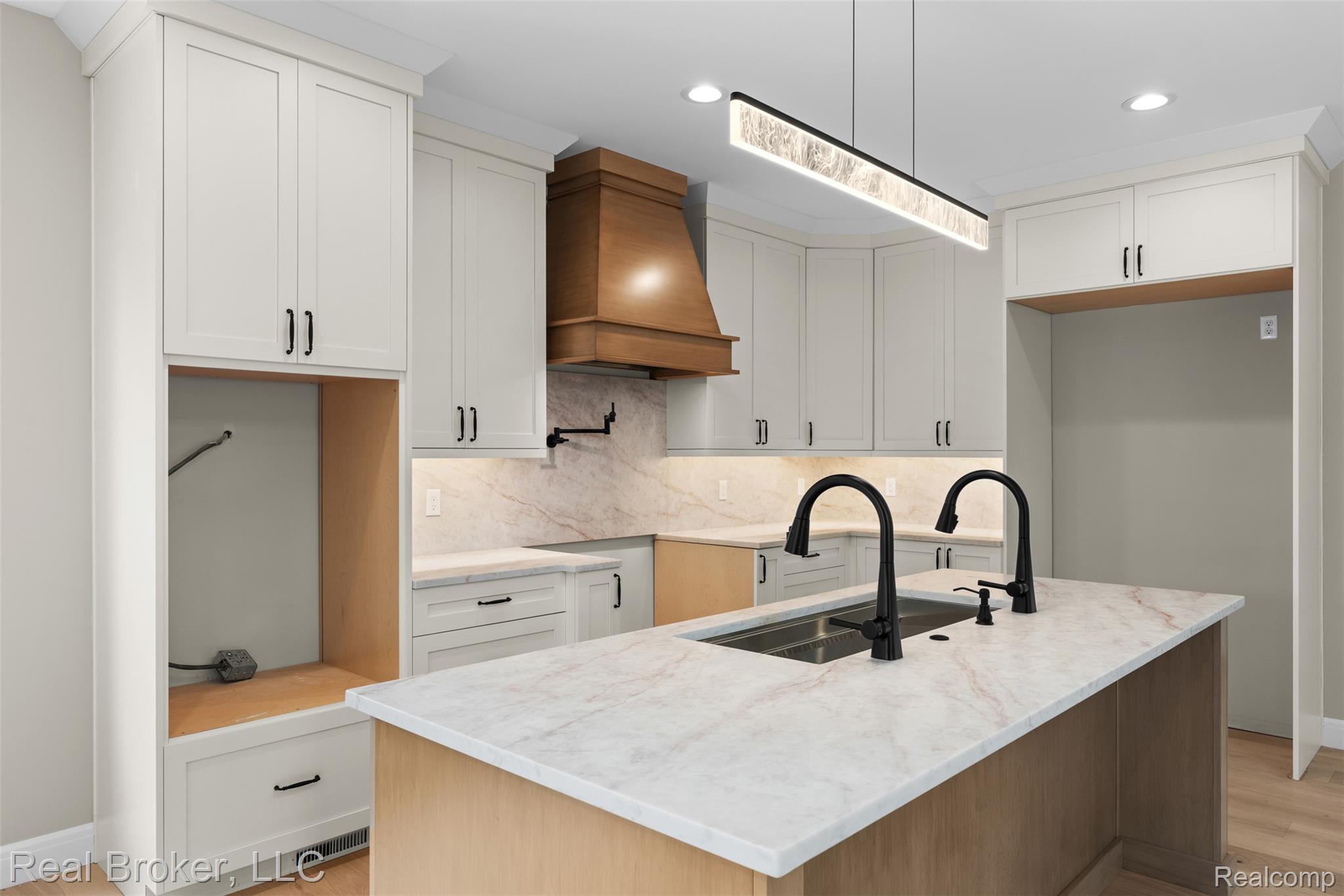 12114 22 Mile Road Utica, MI 48315 - Photo 18 of 70 Kitchen featuring an island with dual matte black faucets, light-toned cabinetry, a wood-finish range hood, recessed lighting, and a linear pendant light fixture