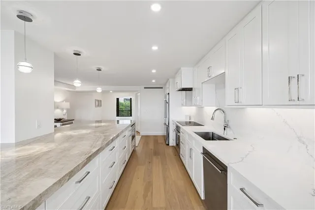 a large white kitchen with a sink and dishwasher a stove top oven with wooden floor
